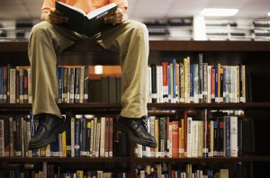 Man Reading Book and Sitting on Bookshelf in Library